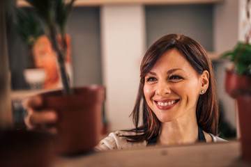 Close-up image of a smiling botanist taking indoor plant from a shelf