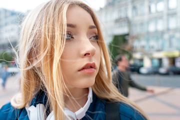 Outdoors Recreation. Teen girl student in denim jacket and headphones walking on urban background looking aside pensive close-up