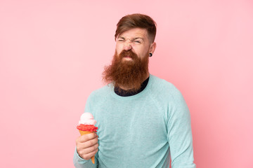 Redhead man with long beard holding a cornet ice cream over isolated pink background making doubts...
