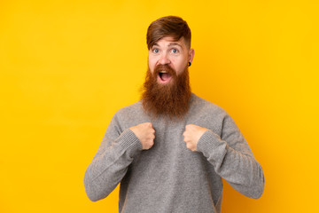 Redhead man with long beard over isolated yellow background with surprise facial expression