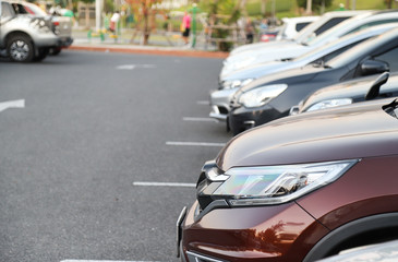 Closeup of front side of dark red  car and other cars parking in outdoor parking lot with natural background in twilight evening.