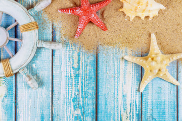 Decorative steering wheel with starfish, seashells on the sandy beach blue wood background