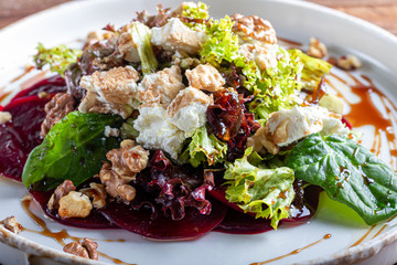 Beetroot carpaccio with walnuts, goat cheese, lettuce and spinach. Dressed with sauce. On a dark...