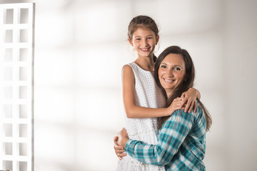 Young cheerful caring mother hugs her pretty positive daughter standing on a white background. concept in a warm relationship between children and parents. Place for advertising