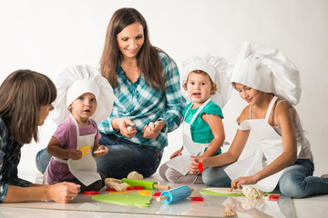 Obraz na płótnie Canvas Charming young mother shows a master class to her cheerful children on the preparation of pastries and cookies. Concept of teaching children to a healthy lifestyle and work since childhood