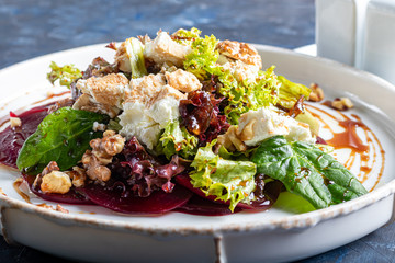 Beetroot carpaccio with walnuts, goat cheese, lettuce and spinach. Dressed with sauce. On a dark background.