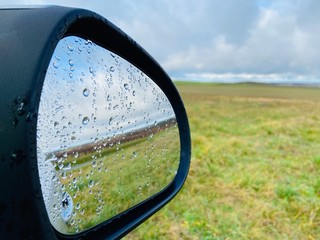 Raindrops on side view car mirror with field background