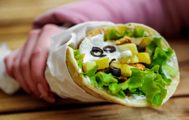 greek meat gyros with tzatziki sauce, vegetables, feta cheese and french fries in woman hand. street food