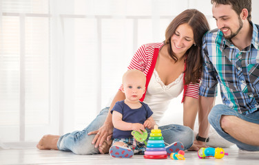 Young positive family, mom, dad and a half-year-old son are sitting on the floor in their cozy living room and spending the weekend together. Family time concept