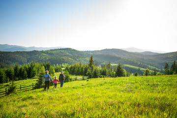 Young mother and two little daughters travelers stand on a slope with a gorgeous view of the hills...
