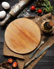Concept of Italian and French cuisine on a dark wooden background. Lettuce, tomatoes, eggs and rolling pin. Background image, copy space