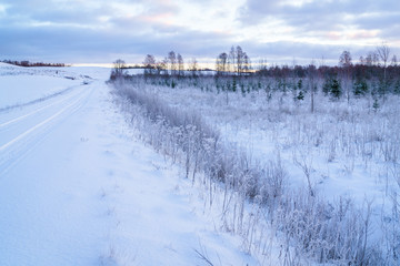 Fototapeta premium Winter morning, country road and fields covered with snow, in the distance you can see a hilly landscape.