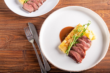 Duck breast with a side dish of potato casseroles, seasoned with pea microgreen with tomato and chili sauce. On a white plate. On a wooden background,