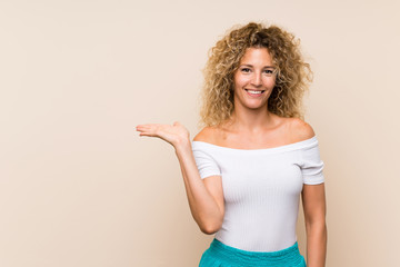 Young blonde woman with curly hair over isolated background holding copyspace imaginary on the palm...