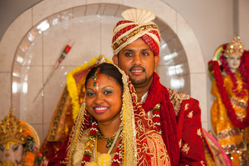 Beautiful happy couple of newlyweds in bright national costumes during the wedding ceremony in a Hindu temple against the background of national gods. World tourism, traditions.