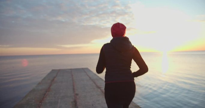 Strong young woman running in morning. Cardio workout training focused female athlete runner in seaside background.