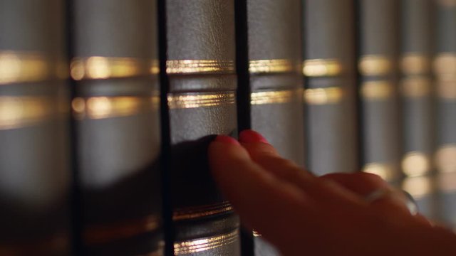 Female hand chooses a book in the library with a luxurious leather binding. 4k