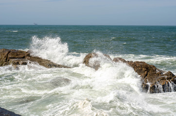 Wave with foam breaking of rock in ocean or sea