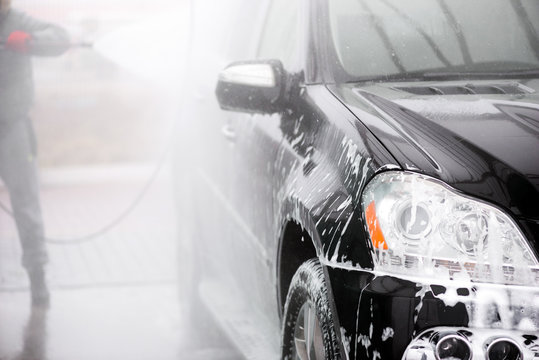 Man washing his car under high pressure water outdoors. - Image with soft focus