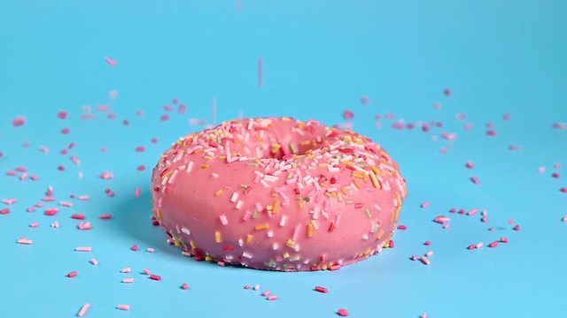 Color toppings sprinke on top of delicious pink donut on blue background. Sweet food and sugar nutrition concept .
