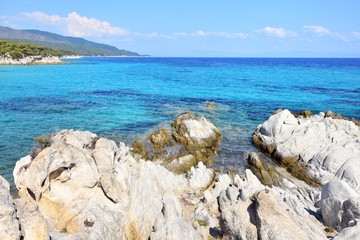 Seascape of rocky beach with azure sea water in sunny day. Amazing natural beach with white stones and turquoise water. crystal clear sea with sun reflection. Halkidiki Greece Blue Flag Beach