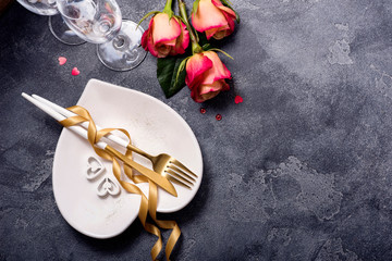 Romantic dinner table setting with roses, champagne glasses, heart shaped plate and golden ribbon,...