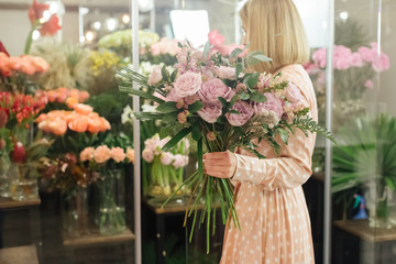 Beautiful smiling female florist in apron arranging bouquet in flower shop