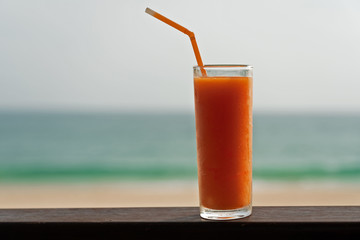 Papaya fruit cold juice glass with tubule on the ocean beach background.