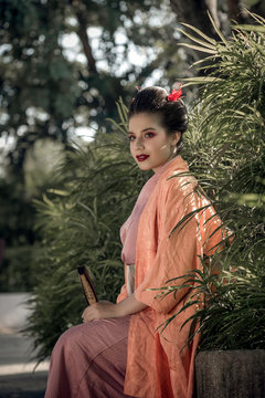 Woman dressed in a geisha costume, sitting in the garden