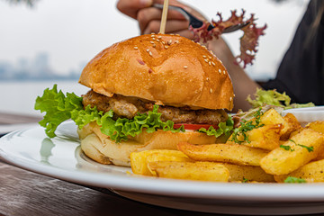 Hamburger with french fries hand with fork in cafe