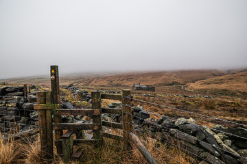 Fototapeta na wymiar Misty and foggy day on the moors showing a stile and a derelict house- Hoof stones height