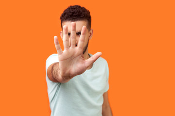 Stop! Portrait of bossy brunette man in white t-shirt standing with outstretched hand hiding his...