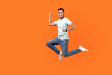 Full length portrait of positive inspired brunette man with beard in sneakers, denim outfit jumping in air or running quickly fast. indoor studio shot isolated on orange background, empty copy space