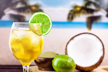 Glass of cold drink, with beach in the background. Refreshing drink, carioca mate tea, made in the city of Rio de Janeiro. Yerba mate drink, with coconut water and lemon. Brazilian summer tourism.