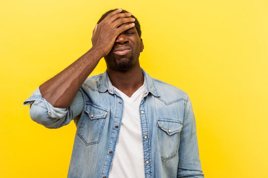 Facepalm, I forgot. Portrait of regretful man in denim casual shirt holding hand on face, feeling sorrow and desperation about failure, his fault. indoor studio shot isolated on yellow background