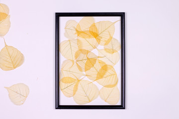 Decorative composition, black photo frame on a white background, yellow leaves. Flat lay, top view, copy space.