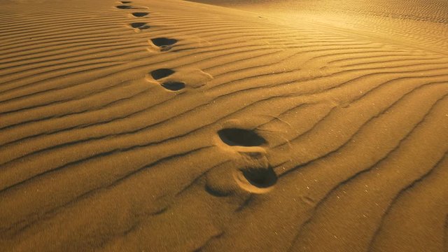 Footprints in the sand in desert at warm sunset lights. Сamera follows footprints in big sand dune. UHD, 4K