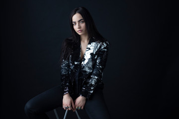 Fototapeta premium Woman with attitude, have long brunette hair in a silver shiny jacket from sequins, with natural makeup, eyebrows, over black background.