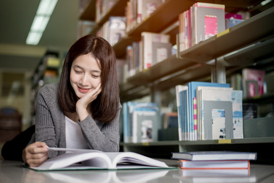 Young girl student laying on the library floor and reading a stack of books,Education concept