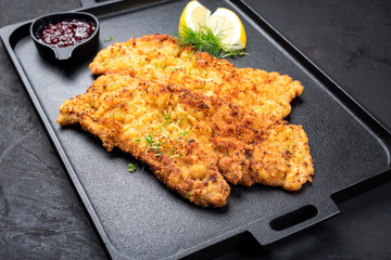 Traditional deep fried Wiener schnitzel from veal topside with cranberry jam and lemon slices offered as top view on a black modern design tray