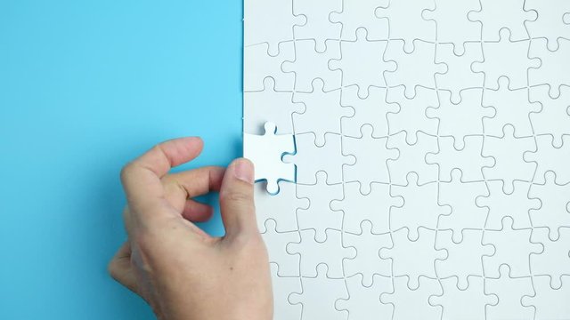 Hand putting the last piece of white jigsaw puzzle on blue background and place for your content