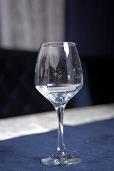 Tableware on table in cafe, focus on wineglass stem . Elegant table setting . Bakal blue background . Empty wine glass.