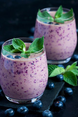 Blueberry smoothie in  glass with mint leaves on dark background
