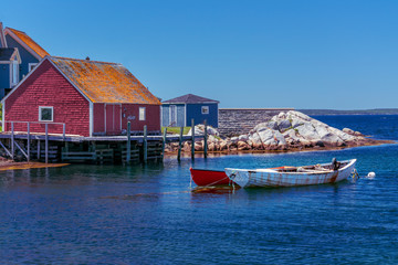 Fototapeta na wymiar Red Fishing Shed in Rural Nova Scotia - On a beautiful serene summer's day a pair of row boats are docked near a red shed on a wharf on Nova Scotia's coast.