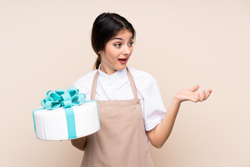 Pastry chef woman holding a big cake over isolated background with surprise facial expression