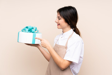 Pastry chef woman holding a big cake over isolated background pointing to the side to present a product
