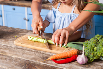 Closeup of mother and child chopping vegetable with knife on board, cooking healthy breakfast...