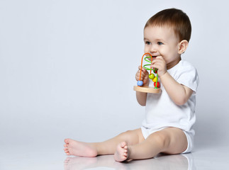 Newborn baby boy toddler holding playing with a multi-colored developing toy for kids, biting it on a gray