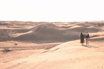 Young couple enjoying the sunset in dunes. Romantic traveler walking on the Sahara desert. Adventure travel lifestyle concept.