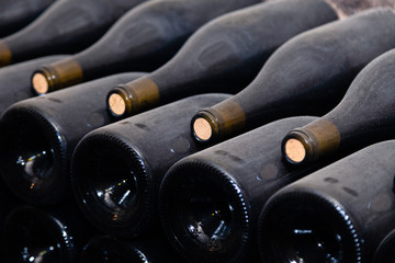 Stacks of wine bottles laying flat in racks in old wine cellar or cave. Concept vault with old rare...